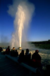 This is a picture of Beehive Geyser is Yellowstone. Water is spewing out from the geyser and people are watching.