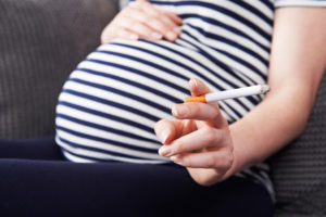 Picture of pregnant woman's belly and hand holding a cigarette.