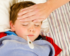 Sick boy laying in bed with thermometer.