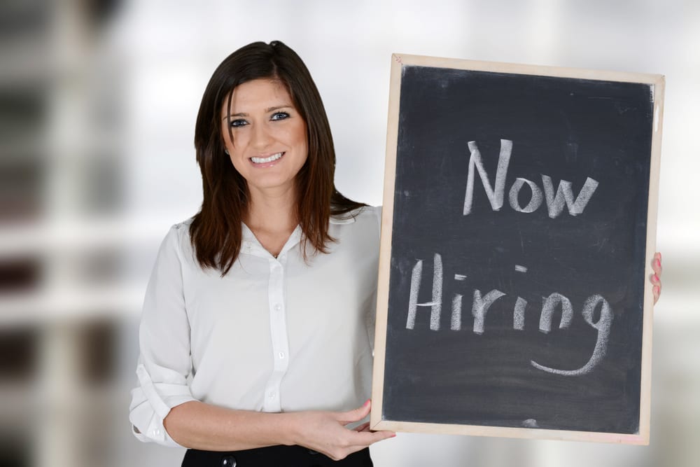 woman holding a now hiring chalkboard sign