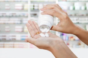 Pills pouring into hand with pharmacy in the background.