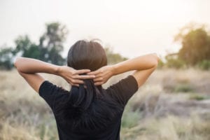 woman in field with hands on head