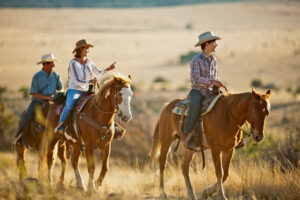 Family on horseback in Western landscape rides together and smiles.