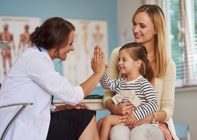 A pediatrician giving a high-five to a young girl, with the mother smiling beside them.